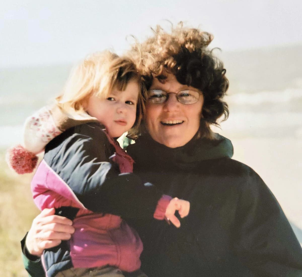 Photo of Katie hugging her young child on a beach.